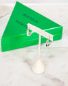 Silver earring stand with two silver earrings in front of a green Bottega Veneta box on a marble surface.