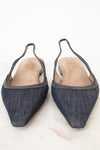 A pair of pointed-toe slingback flats made from dark blue denim, featuring a thin metallic trim along the edge and a light tan insole, photographed on a light marble surface.