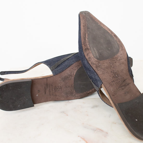 A pair of worn navy blue slingback sandals with pointed toes, shown from the soles and sides, resting on a white marble surface against a white background.
