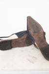 A pair of worn navy blue slingback sandals with pointed toes, shown from the soles and sides, resting on a white marble surface against a white background.