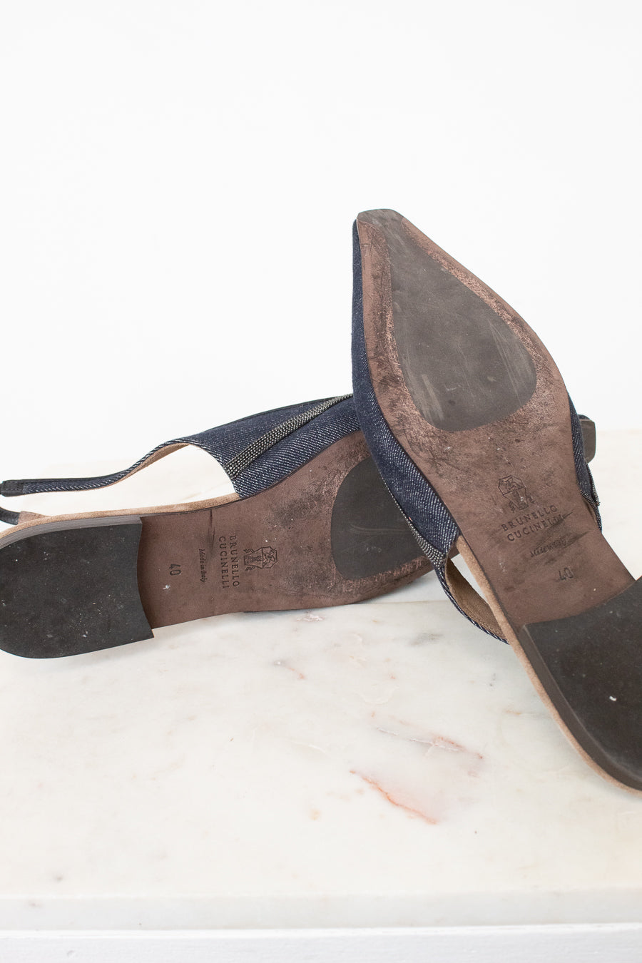 A pair of worn navy blue slingback sandals with pointed toes, shown from the soles and sides, resting on a white marble surface against a white background.