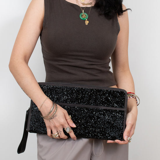 Woman holding a black glittery clutch against a plain background