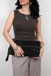 Woman holding a black glittery clutch against a plain background