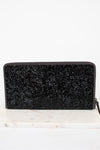 Black glittery clutch bag on a white marble surface with a white background