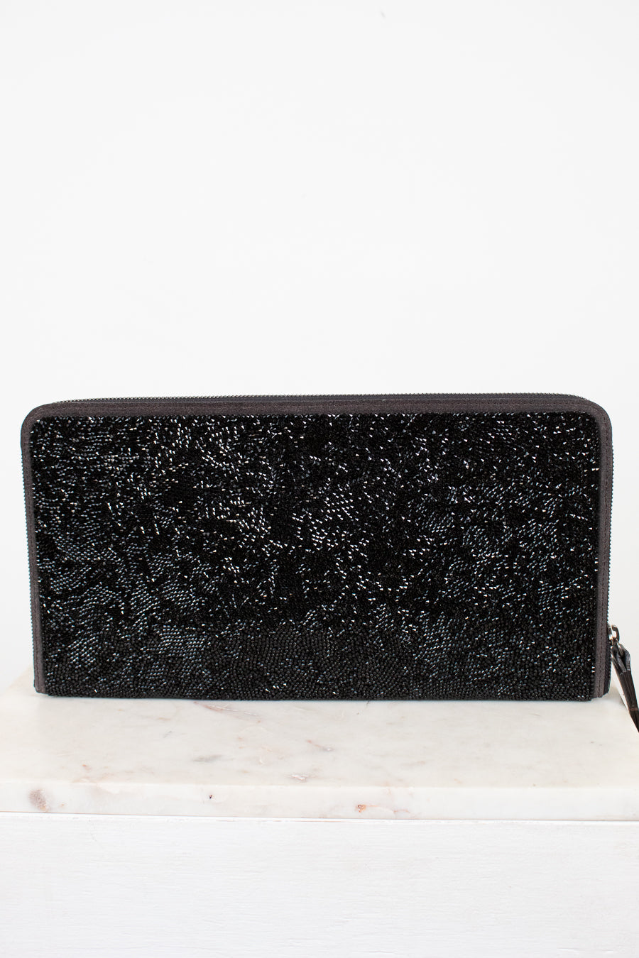 Black glittery clutch bag on a white marble surface with a white background