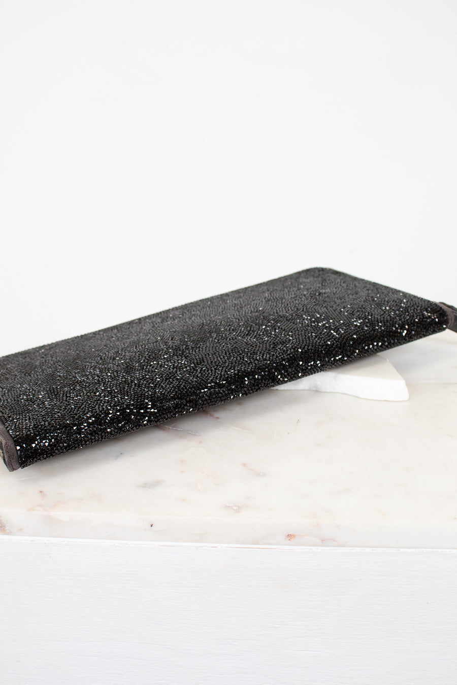 Black glittery clutch bag on a white marble surface