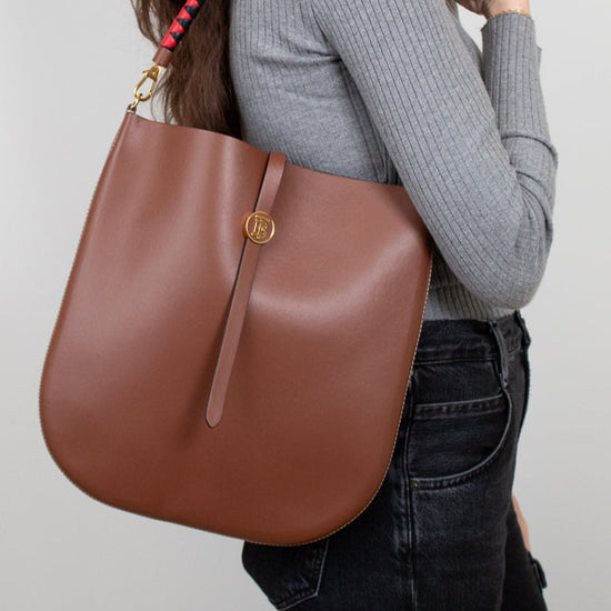 Person wearing a brown leather handbag with a red strap on a plain background