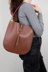 Person wearing a brown leather handbag with a red strap on a plain background