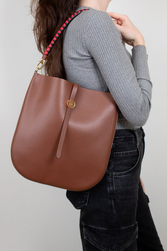 Person wearing a brown leather handbag with a red strap on a plain background