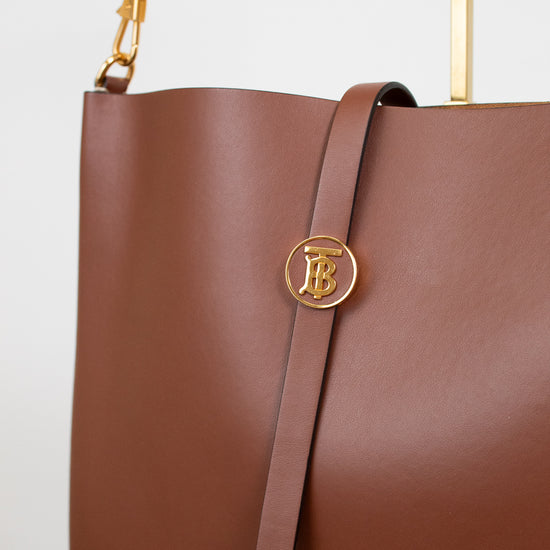 Brown leather handbag with gold logo on a light gray background