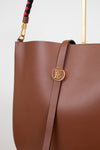 Brown leather handbag with gold logo on a light gray background