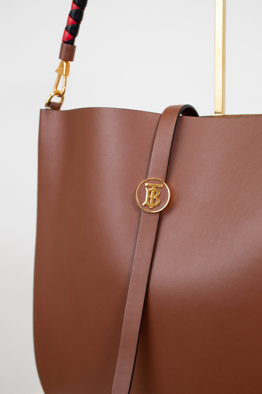 Brown leather handbag with gold logo on a light gray background