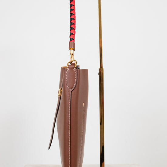 Brown umbrella with a red and black handle on a gold stand against a white background