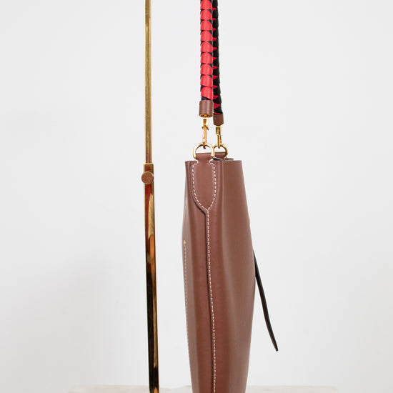 Brown leather umbrella with a red and black handle on a gold stand against a white background