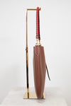 Brown leather umbrella with a red and black handle on a gold stand against a white background
