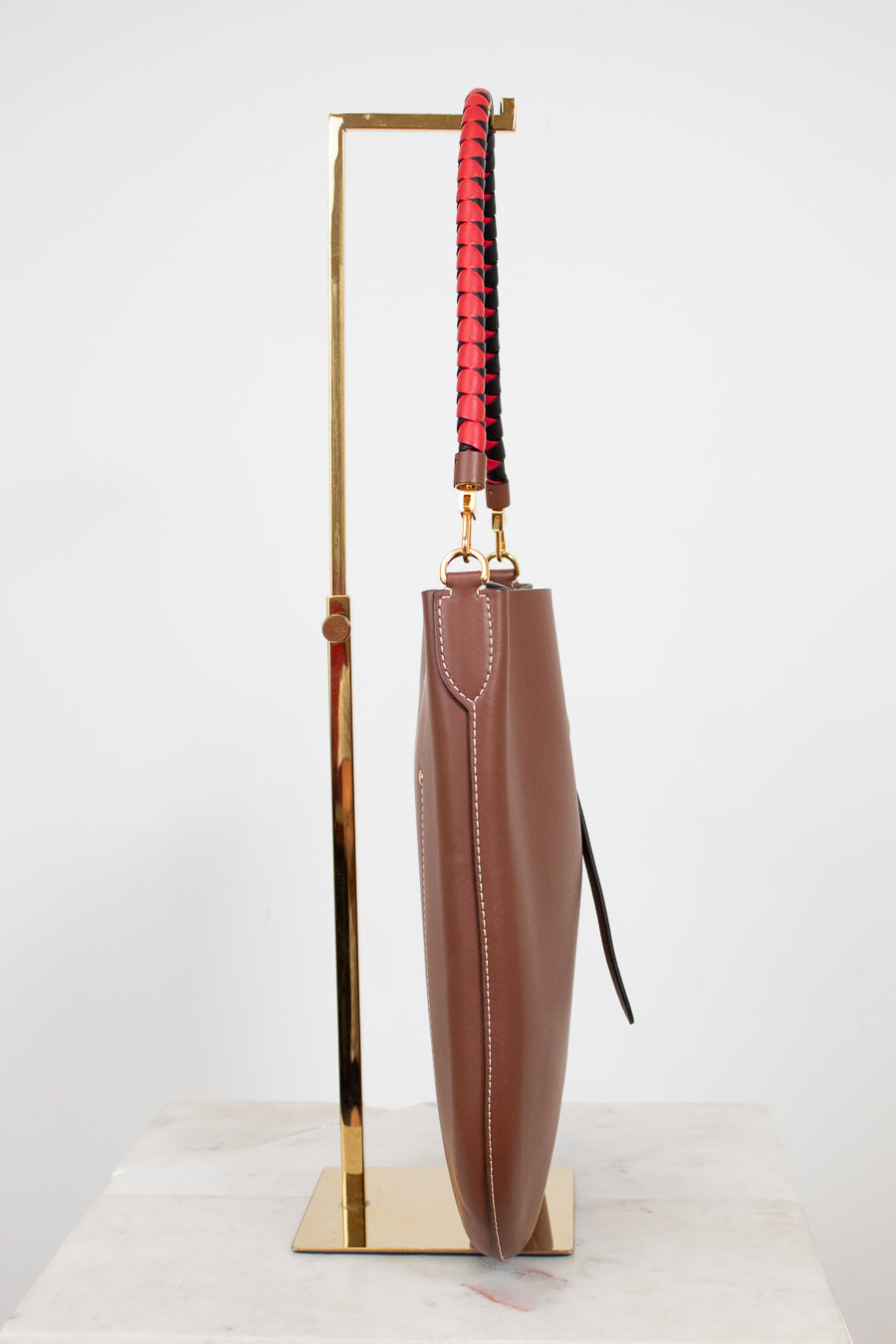 Brown leather umbrella with a red and black handle on a gold stand against a white background