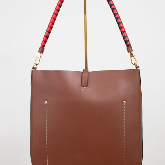 Brown leather handbag with red and black patterned handle on a white background