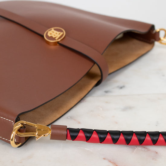 Brown leather handbag with a red and black patterned strap on a marble surface