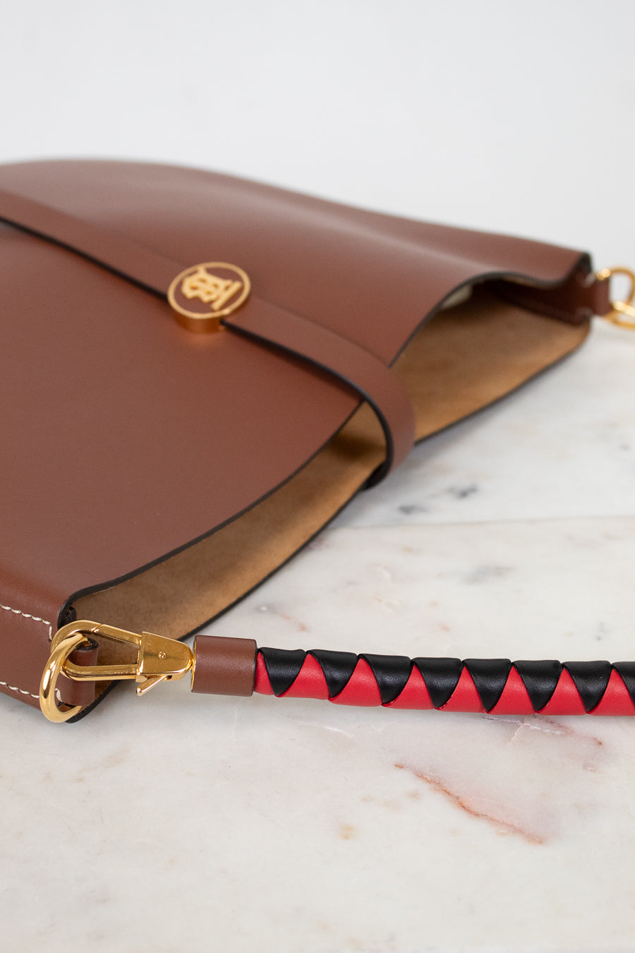 Brown leather handbag with a red and black patterned strap on a marble surface
