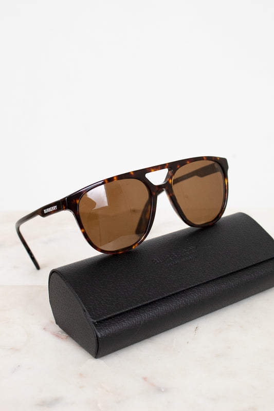 Tortoiseshell sunglasses with brown lenses on a black case against a white background