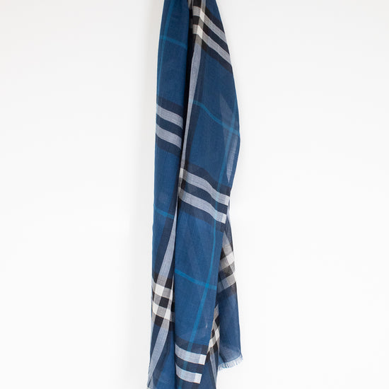 A blue plaid scarf with white and gray stripes, hanging from a small white hook against a plain white wall.