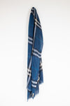 A blue plaid scarf with white and gray stripes, hanging from a small white hook against a plain white wall.