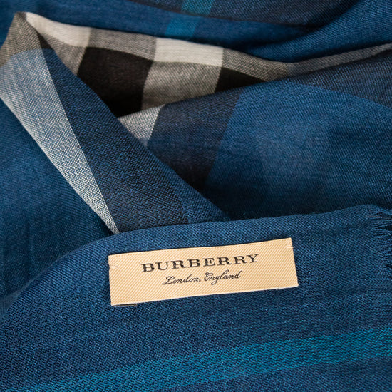 A close-up of a Burberry scarf in a blue plaid pattern with a beige brand label sewn onto it.