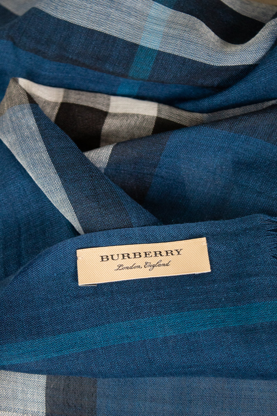 A close-up of a Burberry scarf in a blue plaid pattern with a beige brand label sewn onto it.
