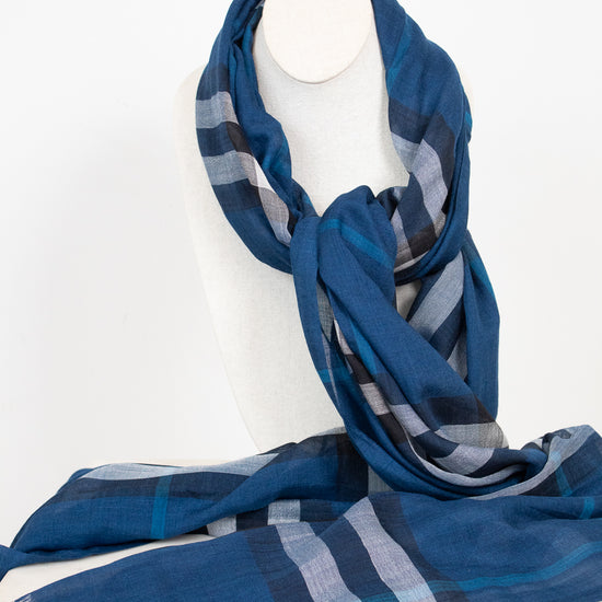 A blue plaid scarf with gray and white stripes, draped on a white mannequin neck against a white background.