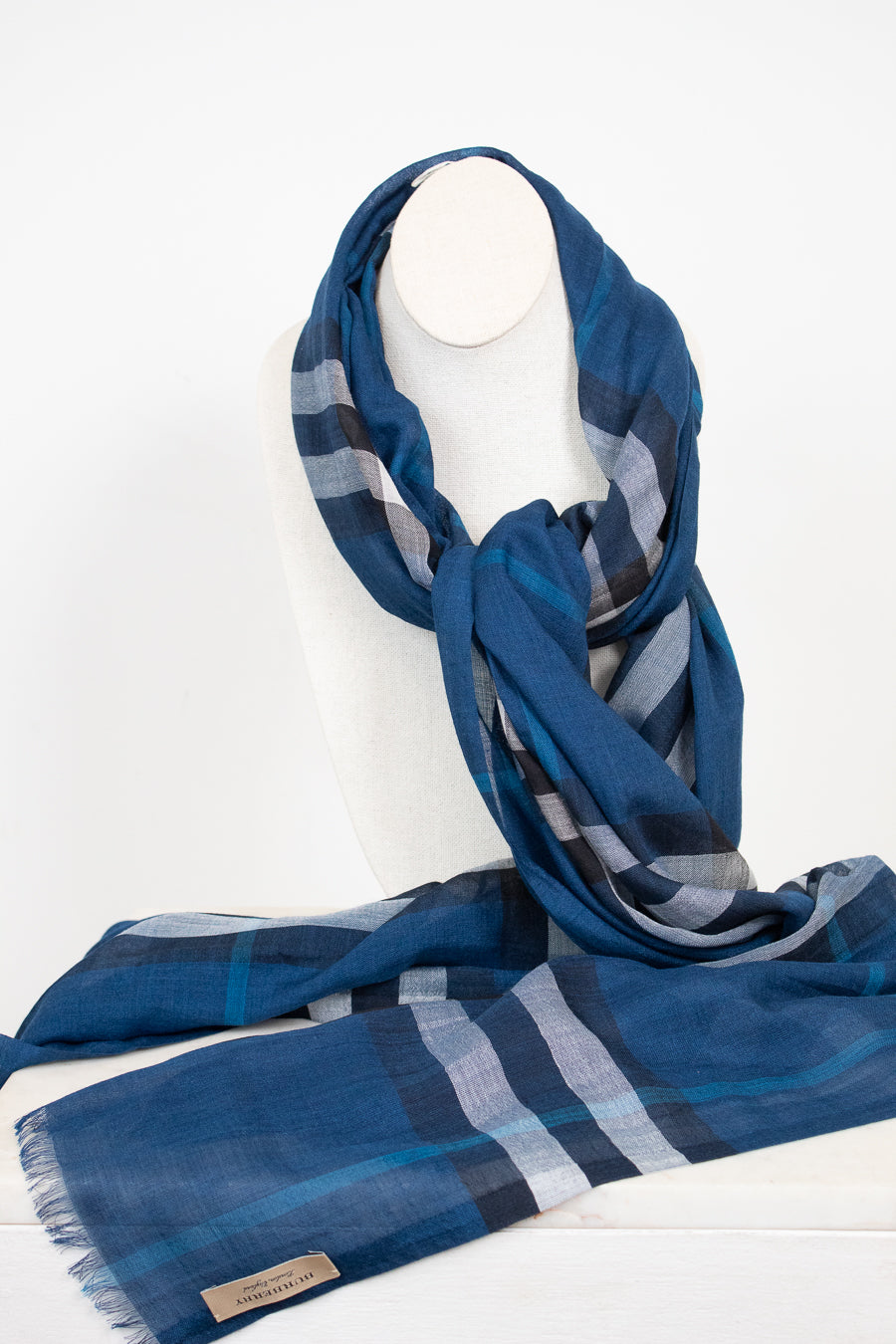 A blue plaid scarf with gray and white stripes, draped on a white mannequin neck against a white background.