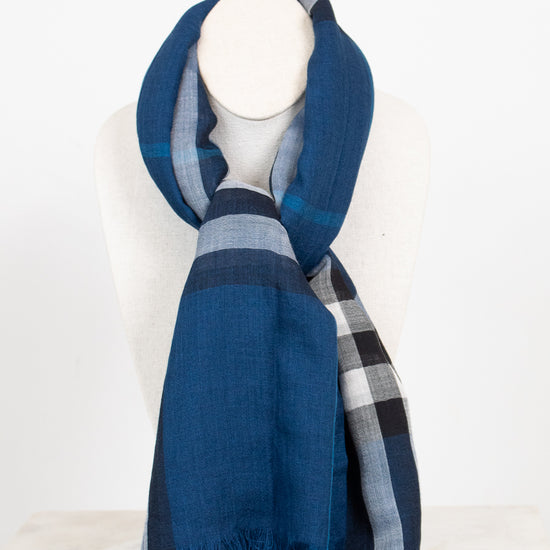 A blue plaid scarf with fringed edges, draped on a white mannequin neck against a clean white background.