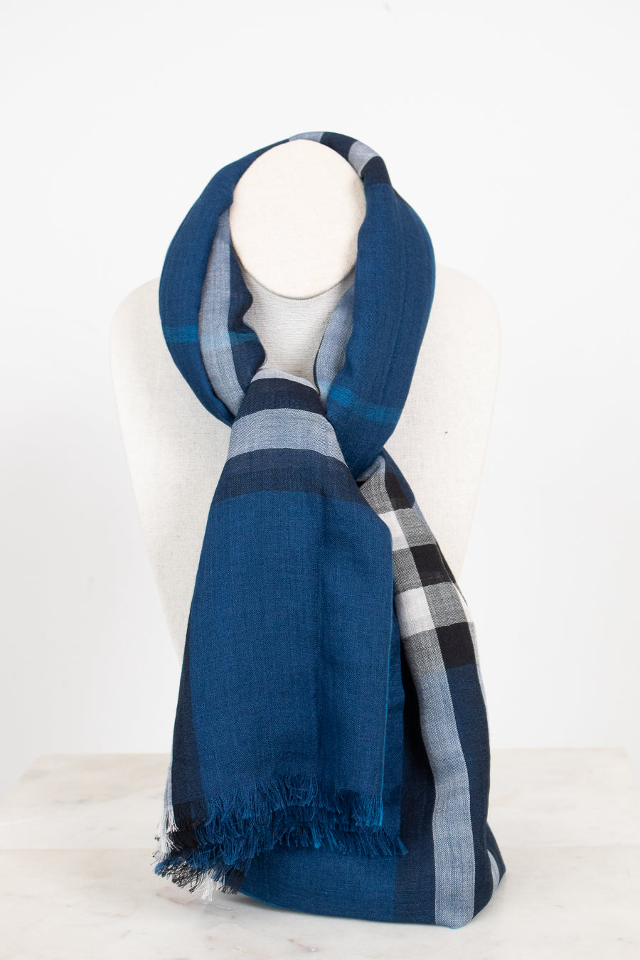 A blue plaid scarf with fringed edges, draped on a white mannequin neck against a clean white background.