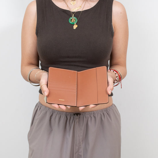Woman holding a brown leather passport holder against a plain background