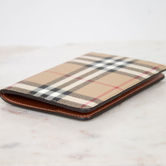 Plaid patterned passport holder with brown leather trim on a light wooden surface