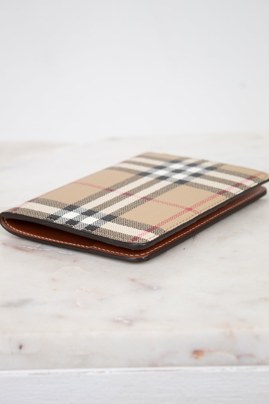 Plaid patterned passport holder with brown leather trim on a light wooden surface