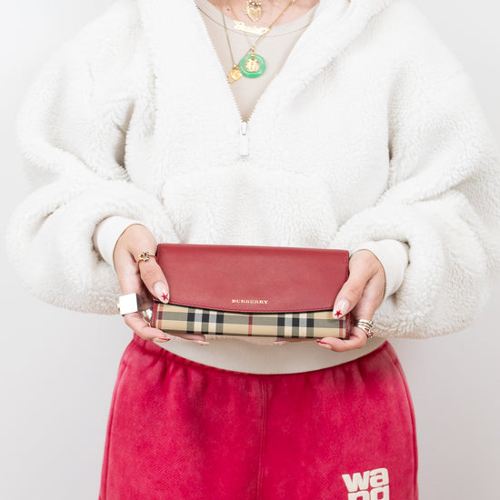 Person holding a red clutch with a visible brand logo against a white background