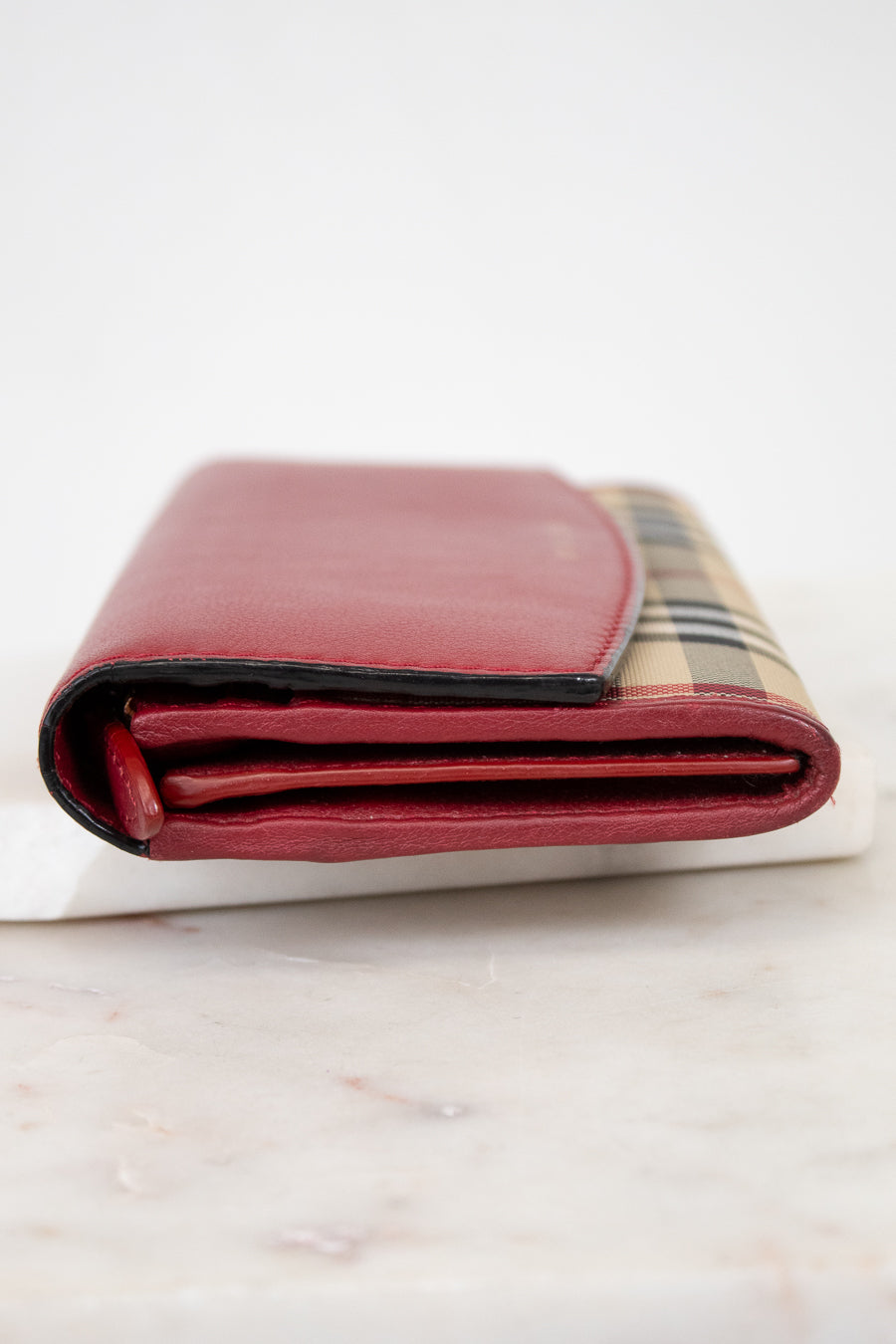 Folded red leather wallet with checkered pattern on a marble surface