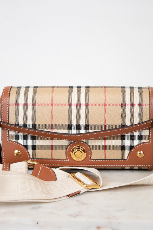 Designer handbag with plaid pattern and brown leather accents on a light wooden surface.