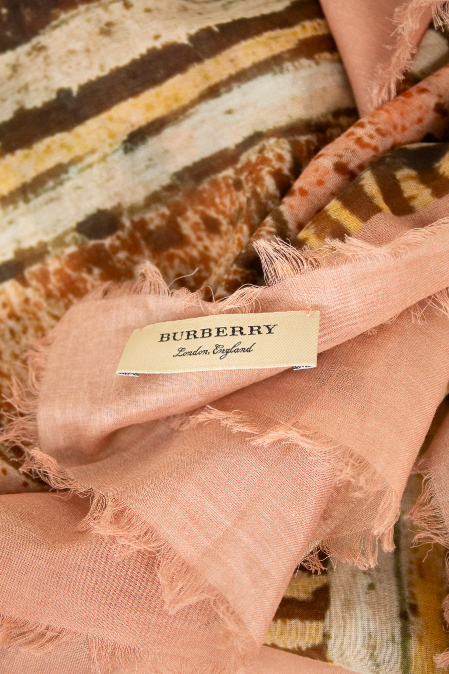 Close-up of tag on light pink and neutral tone scarf with 'Burberry' branded on tag