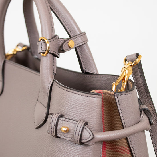 Close-up of a taupe leather handbag with gold-tone hardware and a hint of the signature red and beige check lining visible at the side.