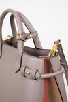 Close-up of a taupe leather handbag with gold-tone hardware and a hint of the signature red and beige check lining visible at the side.