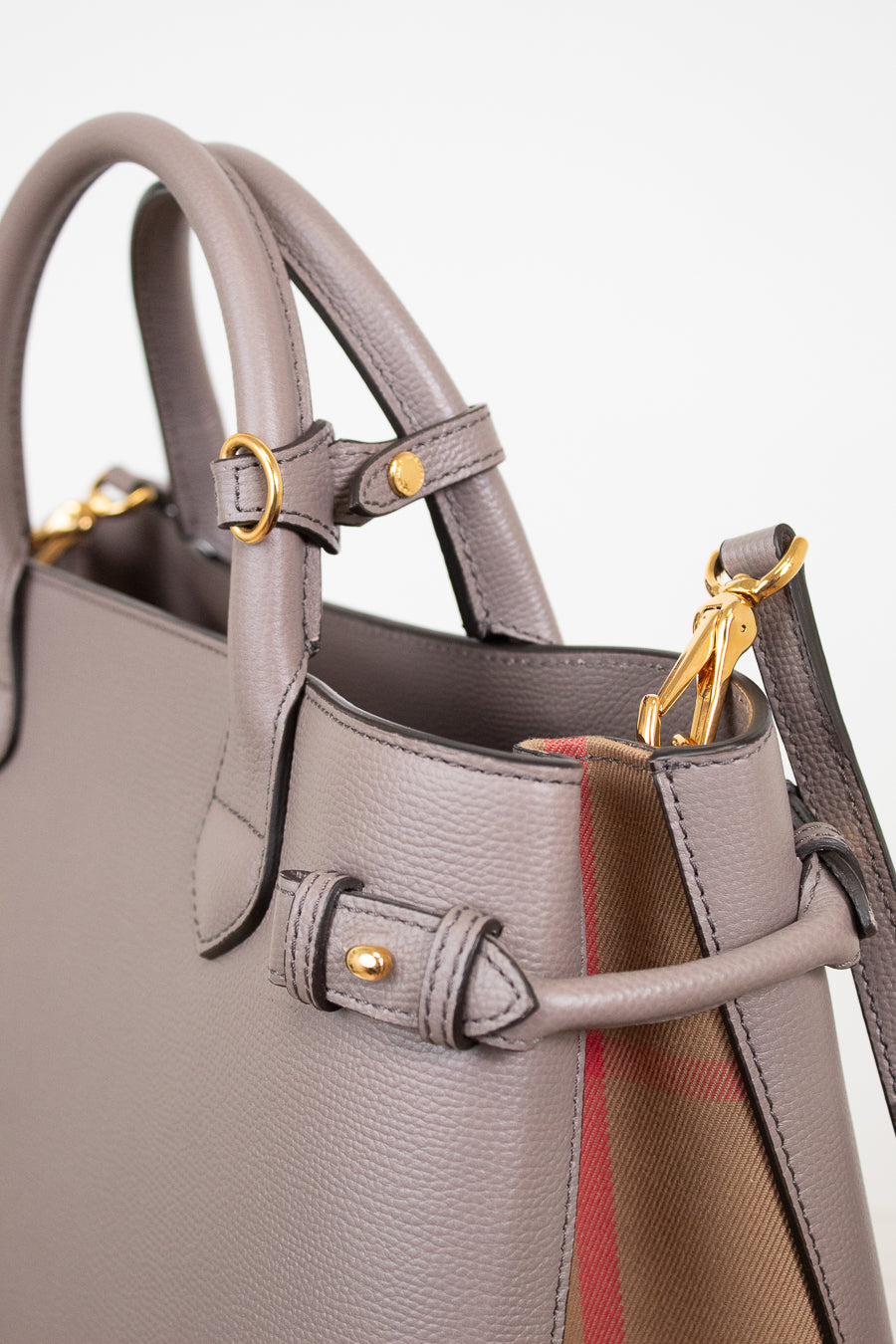 Close-up of a taupe leather handbag with gold-tone hardware and a hint of the signature red and beige check lining visible at the side.