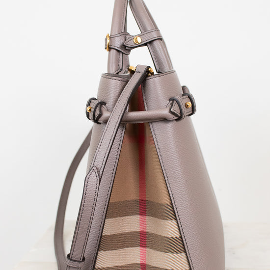 A structured leather handbag in taupe with gold-tone hardware and a signature beige, brown, and red check pattern panel on the front, shown against a clean white background.