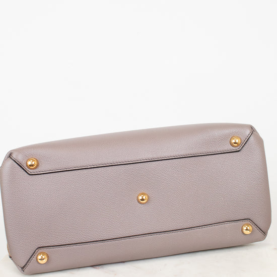 The bottom base of a taupe pebbled leather handbag featuring gold-tone metal studs on the base, resting on a white marble surface against a white background.