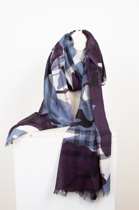 A lightweight scarf with a plaid and abstract camo pattern in purple, slate blue, black, and white, draped over a white mannequin torso on a white display block.