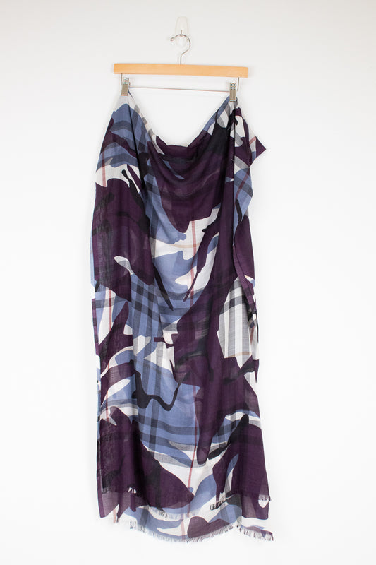 A lightweight draped scarf with an abstract pattern in deep purple, slate blue, and white, hanging from a wooden hanger against a plain white wall.