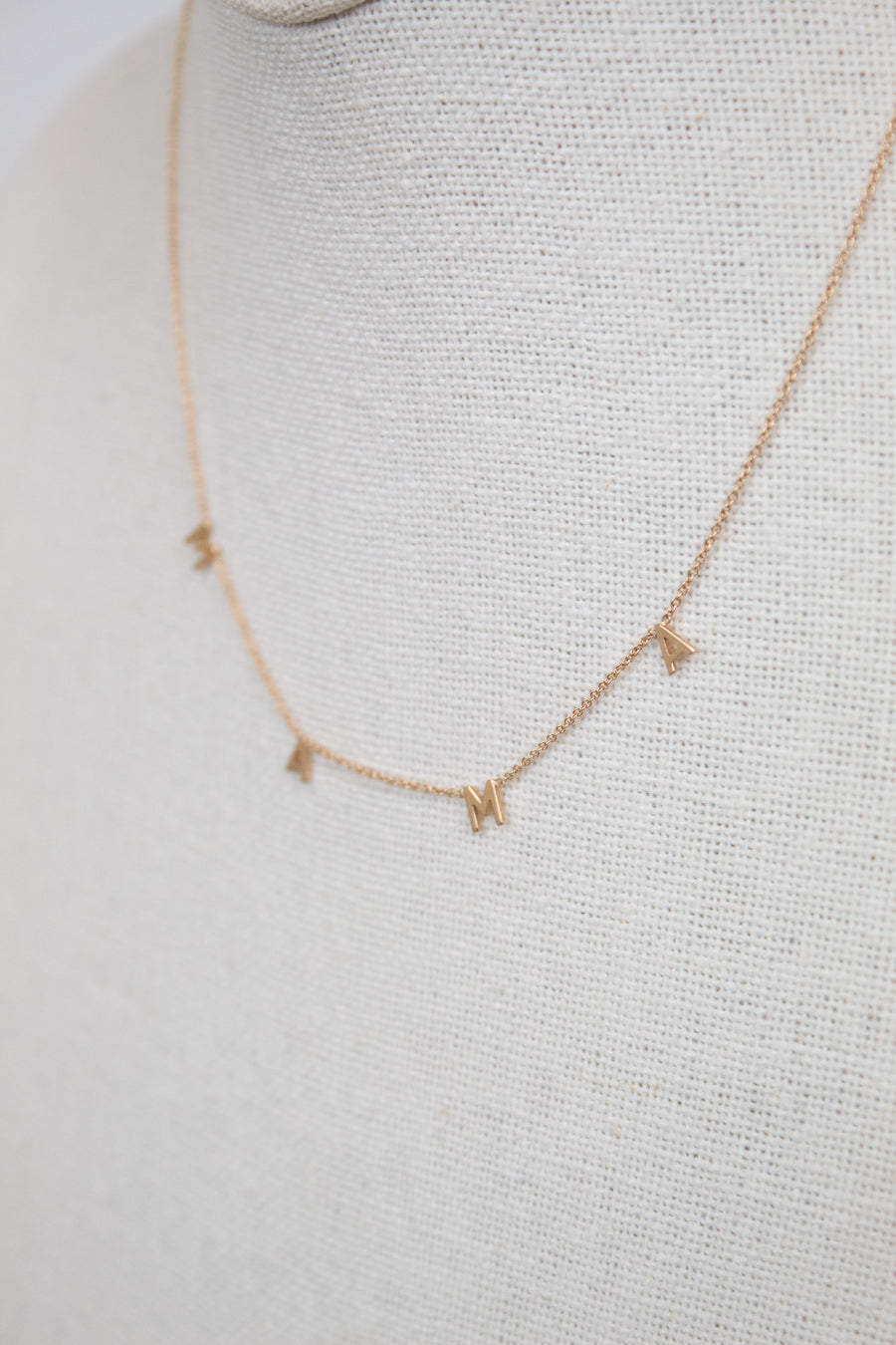 Gold necklace with "MAMA" letters on cream bust