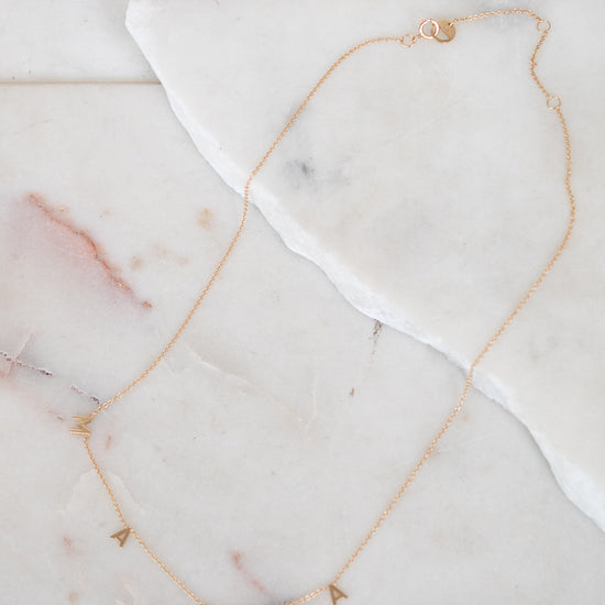 Gold necklace with "MAMA" letters on marble surface