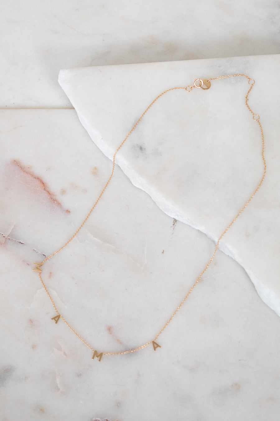 Gold necklace with "MAMA" letters on marble surface