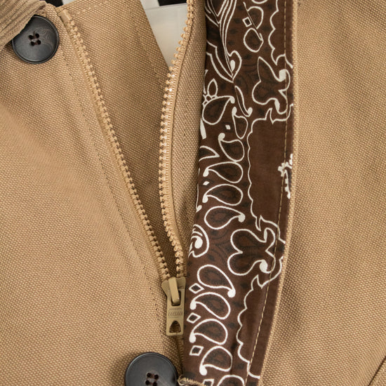 Close-up of a tan jacket with a zipper and decorative band, featuring a brand label.